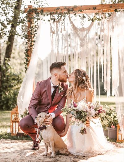 Jaunavedžių pora bučiuojasi priešais medinę arką ir foto sienelę